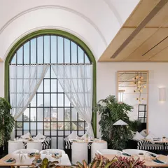 Looking out through the grand arched window at Brassa, which floods the dining area with natural light. The design incorporates abundant greenery, blurring the line between the indoor and outdoor spaces.