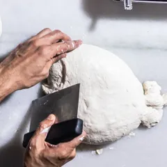 The process of making bread by hand is something I find deeply therapeutic. Here, I'm shaping fresh dough for our house-made ciabatta, ensuring every loaf has the perfect texture and flavor.