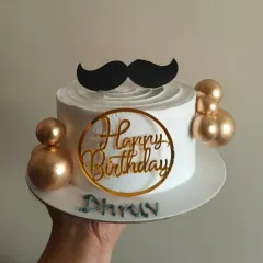 A chic birthday cake for a man, featuring a mustache topper and gold decorative balls.