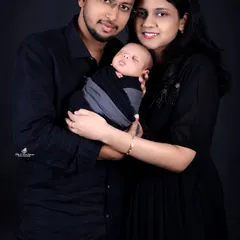 A classic and dramatic family portrait with a newborn. The parents, dressed in coordinating black, hold their sleeping baby against a solid dark background, creating a powerful and intimate photo that focuses solely on the family's connection.