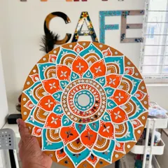 A stunning finished Lippan art piece, held up in the studio. This circular design features vibrant orange and turquoise with detailed mirror work.