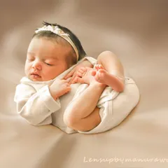 The natural, curled-up poses of a newborn are what make these sessions so special. This portrait captures that fleeting flexibility in a simple, elegant outfit, highlighting the baby's delicate form against a soft, neutral backdrop.
