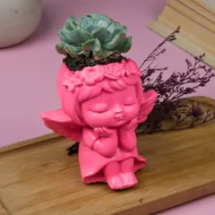 This sweet angel planter is perfect for a small succulent. The vibrant pink color and serene expression make it a charming addition to a desk or shelf.