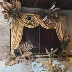 This "Arabic Night" themed seating area features a beautiful peacock wicker chair as a focal point. The backdrop of gold drapes and pampas grass arrangements creates a perfect photo opportunity.