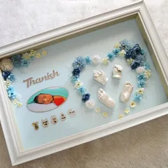 For baby Thanish, I created this heart-shaped floral arrangement using blue and white flowers around his pure white casts. The design includes his photo and birth details, all within a clean white frame.