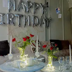 A romantic birthday surprise at home, with "Happy Birthday" foil balloons, red roses, and candles creating a warm and loving atmosphere.