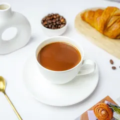 A cup of coffee styled with a croissant and coffee beans in a sophisticated, minimalist setting.