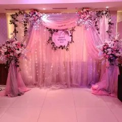 I design elegant backdrops for special occasions like Women's Day. This setup features soft pink draping, twinkling fairy lights, and beautiful floral arrangements, creating a sophisticated and celebratory atmosphere.