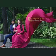 This magenta flying tail gown adds a vibrant pop of color to any setting. Here, the long train is tossed to create a wave of fabric, demonstrating its potential for dynamic couple maternity photos in a lush garden.