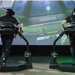 A view from behind shows participants physically running on the Virtuix Omni platforms to move their avatars in the game. This is a full-body experience that combines physical activity with virtual gaming.