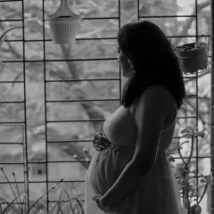 A quiet, contemplative black and white photo of the mother-to-be looking out a window, capturing a moment of peaceful reflection at home.