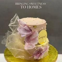 A two-tiered "Congrats" cake designed with soft, ethereal textures. The cake is wrapped in translucent, edible fabric and adorned with delicate, hand-painted floral elements and small pearls for a touch of elegance.