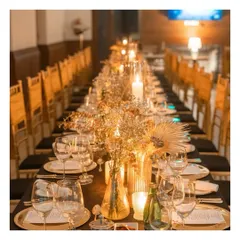 An immaculately set long table awaits guests for an evening of fine dining. The warm glow of candles, gold charger plates, and elegant floral arrangements create an atmosphere of intimate luxury, perfect for a milestone celebration or corporate gala.