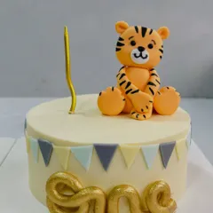 A sweet and simple first birthday cake featuring a cute, handcrafted tiger topper. The soft colors and clean design are perfect for celebrating your little one's big milestone.
