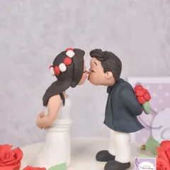 A sweet and simple anniversary cake topper. This kissing couple was hand-sculpted from fondant, complete with a tiny bouquet of red roses, perfect for celebrating a first anniversary.
