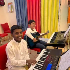 Our classes often have students learning different instruments side by side. Here, you can see one student practicing on the keyboard while another is on the acoustic guitar, creating a dynamic and collaborative learning space.