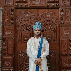 A confident and happy portrait of the groom in his traditional wedding attire, standing before an ornate wooden door.