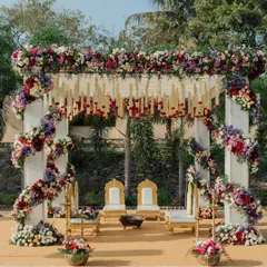 An outdoor wedding mandap that feels both grand and deeply connected to nature. We used a profusion of colorful, fresh flowers to create a vibrant arch, complemented by traditional seating and hanging floral strings, all set against a beautiful natural backdrop.