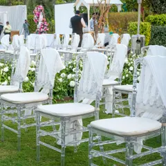 Chic and elegant seating for a sundowner event. Transparent Chiavari chairs are adorned with delicate white drapes, adding a touch of sophistication.