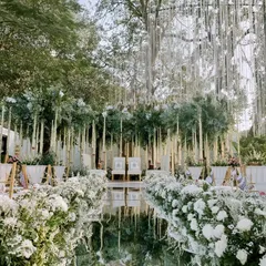 An all-white wedding aisle that is both grand and serene. We lined the mirror walkway with dense white chrysanthemums and hung floral strings from the trees to create this heavenly path.