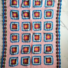 The Lydia blanket laid out flat to show the full pattern. The design features floral squares set against a soft pink background, all framed by a lovely rosebud border.