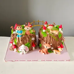 This enchanting woodland-themed cake set was designed for a joint celebration. It features two cakes that form a scene with a bridge, decorated with hand-sculpted foxes, deer, a bunny, and a little explorer.