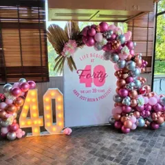 A chic 40th birthday party with the theme "Life Begins at Forty." This decoration includes a beautiful pink, silver, and rose gold balloon arch, a custom backdrop, and large light-up marquee numbers.