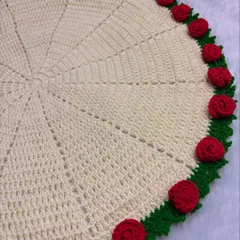 The rose blanket laid flat to show its full 25-inch circular design. The border is adorned with detailed red crochet roses, making it a stunning throw or baby blanket.