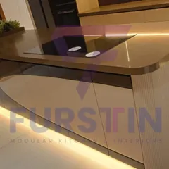 A close-up of the curved kitchen island, showcasing the flawless integration of the induction cooktop into the countertop. The rounded edges soften the design, and the under-island lighting adds a dramatic, floating effect.