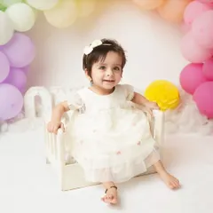 A beautiful, bright smile from the one-year-old. The pastel rainbow balloon arch creates a cheerful and celebratory backdrop for her first birthday photos.