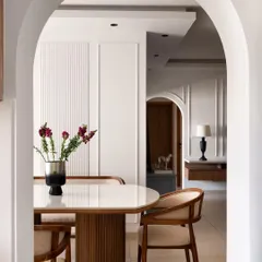 A beautiful arched view into the dining room, highlighting the elegant fluted dining table and classic wall molding. This architectural element was added to create a sense of grace and separation between the living and dining areas.