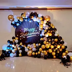 A grand retirement party backdrop with a cascade of black, gold, and white balloons and a custom "Happy Retirement" sign.