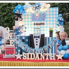 This large-scale Boss Baby setup for Sidanth's first birthday includes multiple character cutouts and a classic blue gingham backdrop. The decor is complete with a "BABY" block display and a tuxedo-themed photo banner.
