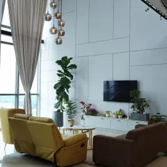 The full view of this double-height living room highlights the floor-to-ceiling windows and sheer curtains that flood the space with natural light, creating a bright and airy atmosphere.