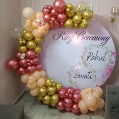 For your engagement or ring ceremony, I can create a personalized backdrop like this one. It features a custom-printed circular board with the couple's names, framed by a beautiful organic balloon arch in shades of rose, gold, and peach for a perfect photo opportunity.