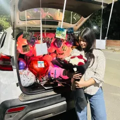 The birthday girl's happy reaction to her personalized car trunk surprise, complete with balloons and a bouquet of flowers.