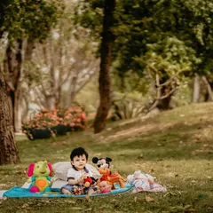 An outdoor portrait of a baby boy enjoying a picnic on the grass with his favorite toys. Including familiar items like stuffed animals can help a child feel comfortable and allows me to capture their natural, happy expressions.