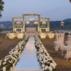 For a more elegant and sophisticated affair, I designed this stunning riverside engagement stage in Jim Corbett. The combination of white floral frames, grand chandeliers, and a clean white aisle creates a breathtaking focal point against the natural backdrop.