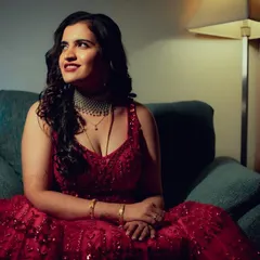 An indoor portrait of a woman in a beautiful red gown, bathed in soft, moody lighting. The mix of cool and warm tones adds a modern, cinematic feel to the shot.