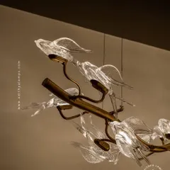This horizontal chandelier features a flock of glass birds perched on a branch, as if in mid-flight. It's a perfect statement piece for suspension over a long dining table or in a living room, adding a dynamic and natural element.
