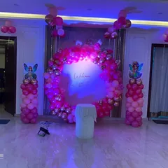 A beautiful "Welcome Our Little Princess" setup in a living room, illuminated with purple lighting. The pink and gold balloon ring creates a glamorous photo backdrop for your home party.