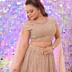 A client posing against a glittering backdrop in the champagne gold lehenga, looking ready for a party.