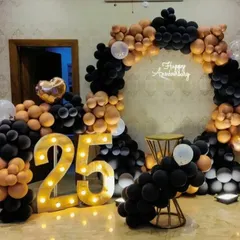 A stylish 25th anniversary setup with a circular organic balloon arch in black and rose gold, paired with illuminated marquee numbers. This design is modern, elegant, and highly photogenic.