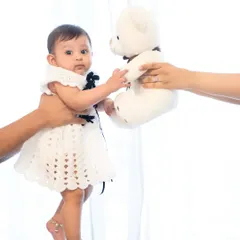 A creative and sweet portrait against a bright white background. Parent's hands hold the baby and a teddy bear, creating a playful interaction and a memory of how small she once was.