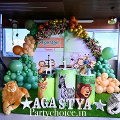 A safari-themed decoration set up on a balcony. This arrangement features a lush green and gold balloon arch, a personalized backdrop, and plush animal toys like a lion and tiger to create a cozy jungle corner.