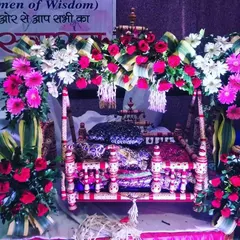 A close-up of a decorated jhula for Ladoo Gopal. The cradle is adorned with bright pink roses and white gerberas, ready for the Janmashtami festivities.