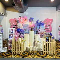 A magical unicorn-themed first birthday celebration. This setup features large butterfly wing cutouts, pastel balloon decorations, unicorn balloon pillars, and a full set of props including a picket fence and 'BABY' blocks.