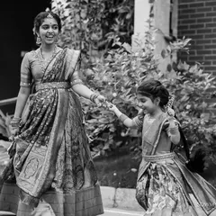 A lovely black and white candid of two sisters in traditional dress, holding hands and walking together. This image captures the simple beauty of their bond and movement.