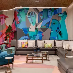 A cubist-style mural in a basement lounge, featuring abstract faces and forms in a cool blue and green palette.