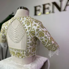 This blouse is a perfect example of my passion for detail. For my client Jhansi, I crafted this piece with intricate gold zardozi embroidery on a white raw silk base, adding a modern touch with a pearl-draped open back and sparkling crystal tassels on the sleeves.